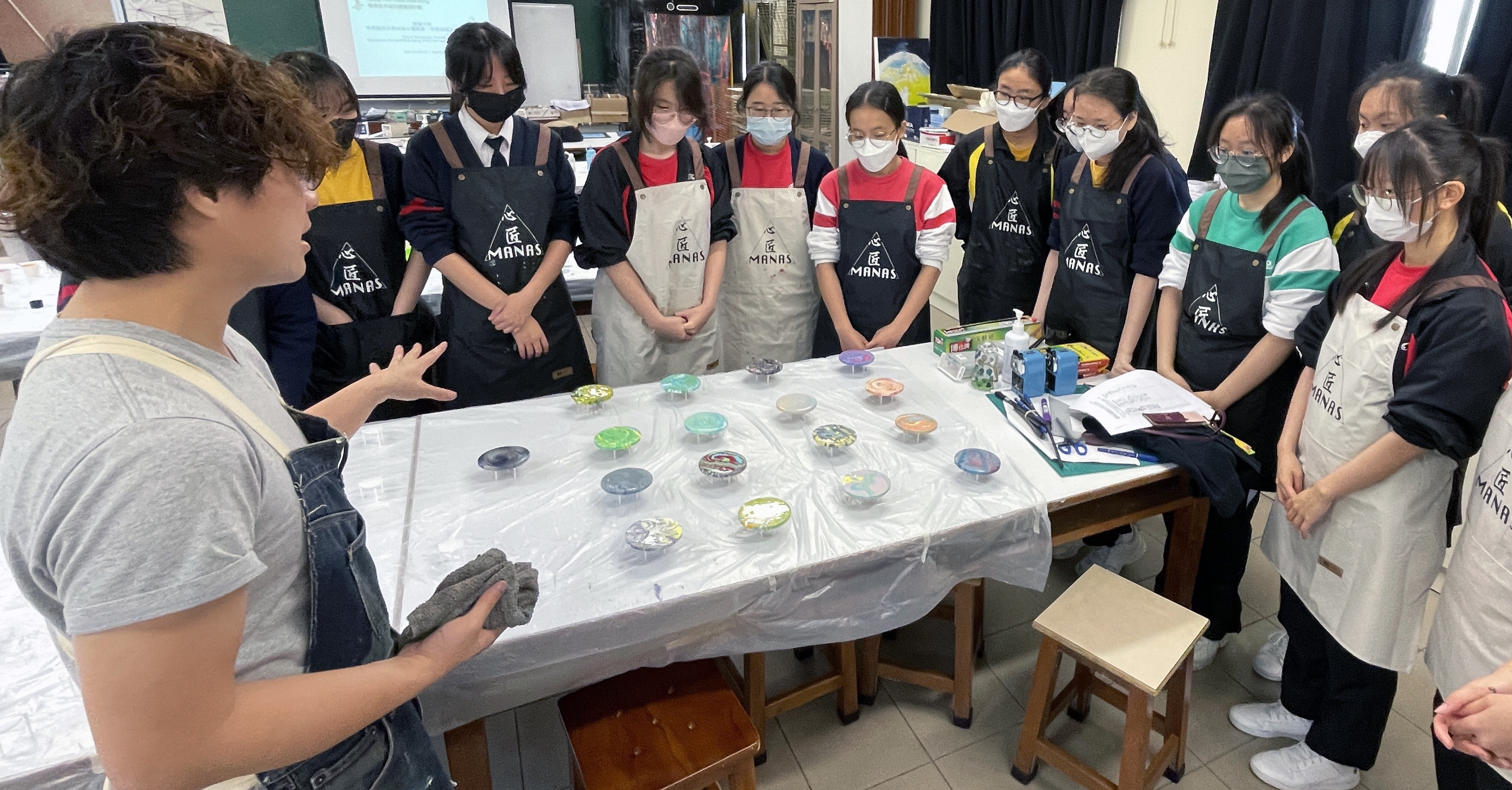 A group of people wearing masks and standing around a tableDescription automatically generated